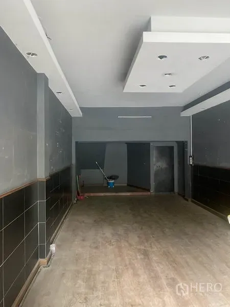 Shophouse for rent in Watthana, Bangkok - Ground-floor retail hall with recessed lighting, dark walls and deep layout leading to a back room