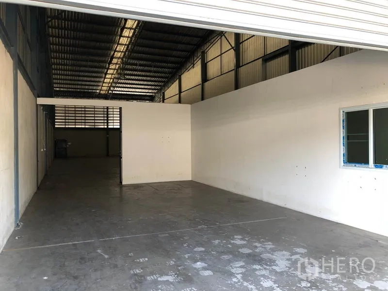 Warehouse for rent in Mueang Samut Prakan, Samut Prakan - Loading area leading to partitioned office beneath metal roof, wide entry for vehicles.