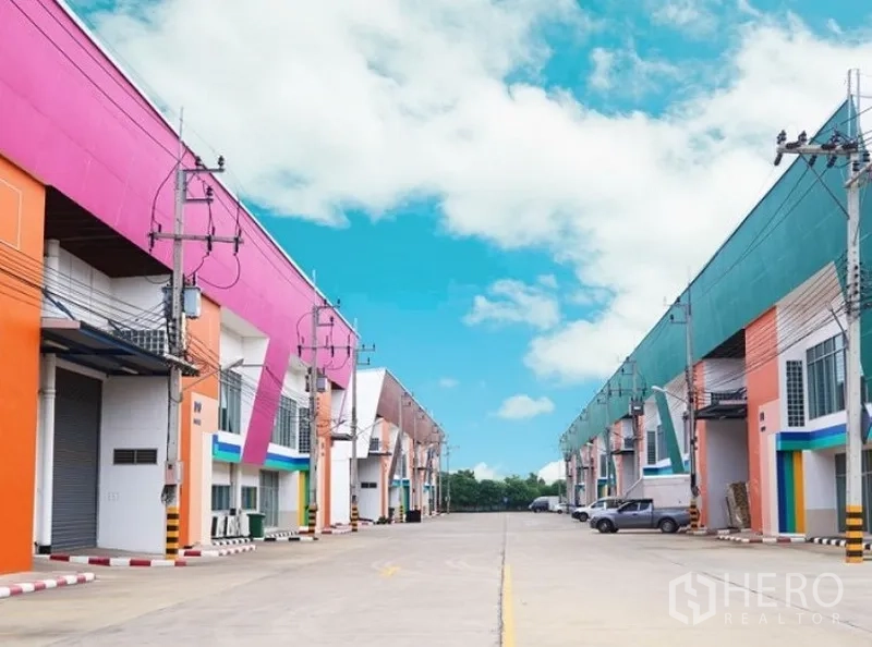 Factory for rent in Mueang Samut Sakhon, Samut Sakhon - Wide internal road between rows of industrial warehouses with loading bays and power lines.