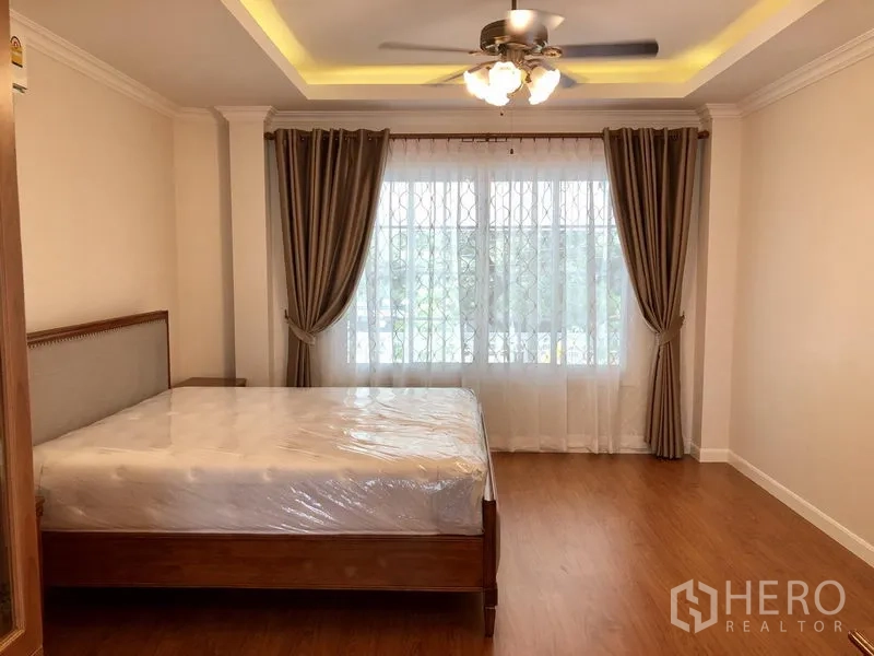 Detached House for rent in Mueang Samut Prakan, Samut Prakan - Spacious master bedroom with tray ceiling, ceiling fan, large window and wood floors.