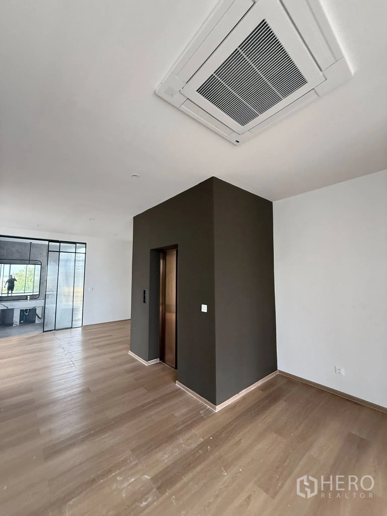 Home Office for rent or sale in Lat Phrao, Bangkok - Ceiling cassette air-conditioning above the lift core in a spacious room with wood floors.