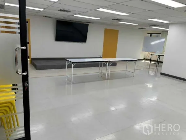 Office Space for rent in Khlong Toei, Bangkok - View through a glass door to a multipurpose office with TV, stage, whiteboard and foldable tables.