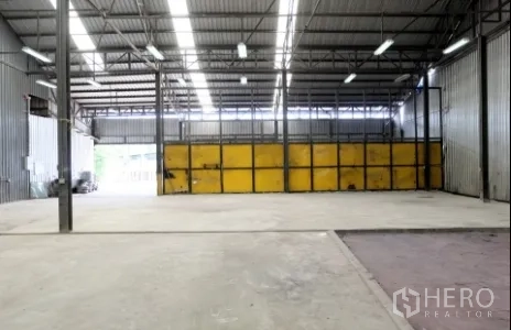 Warehouse for rent in Pak Kret, Nonthaburi - Deep warehouse floor leading to a yellow sectional door and rear loading zone.
