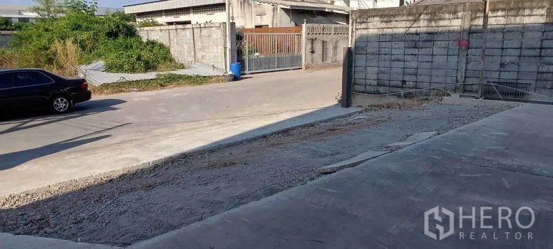 Warehouse for rent in Bang Khun Thian, Bangkok - Concrete ramp and street access leading to a secure industrial compound entrance.
