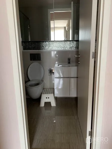 Condominium for rent in Watthana, Bangkok - Modern bathroom with toilet, vanity sink, mirror and tiled flooring.