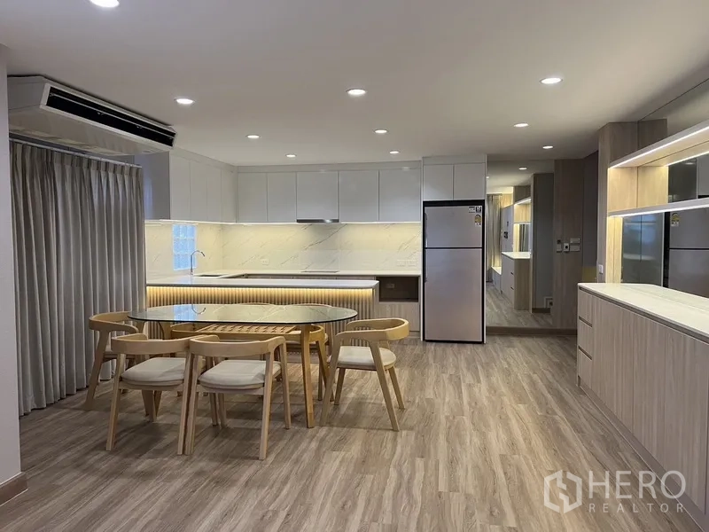 Detached House for rent in Bang Rak, Bangkok - Wide open kitchen with glossy cabinets, under-cabinet lighting, and a dining set on wood floors.