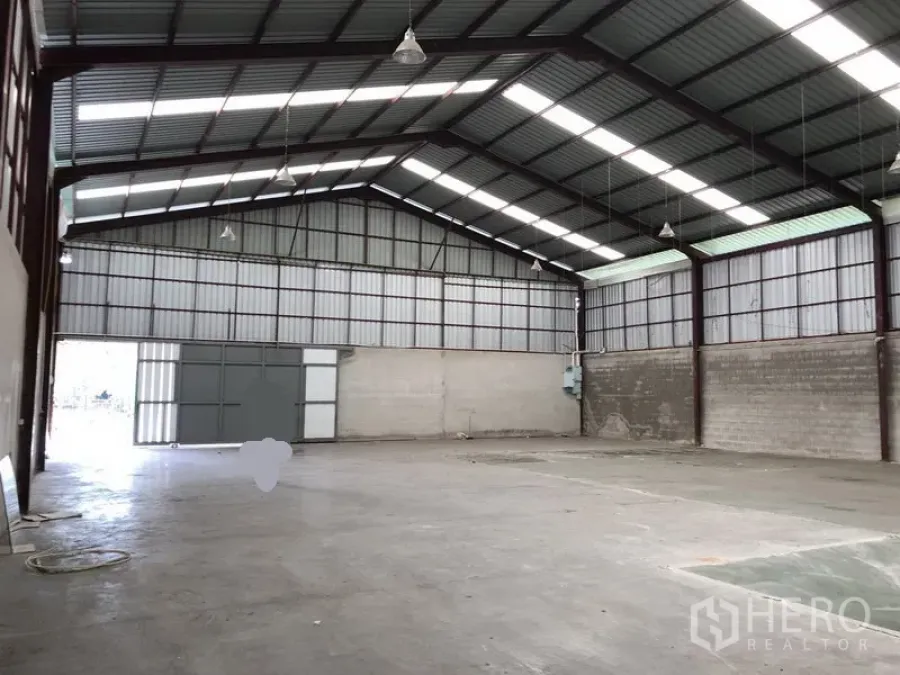 Warehouse for rent in Bueng Kum, Bangkok - Open-plan warehouse view showing clear-span space, large entry doors, and utility panel on the wall.