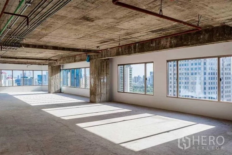 Office Space for rent in Watthana, Bangkok - Sunlit unfinished office space with multiple windows and exposed services facing Bangkok skyscrapers.