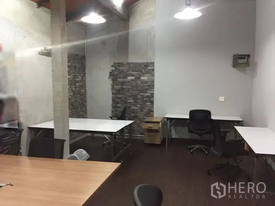 Office Space for rent in Khlong Toei, Bangkok - Open-plan office with white workstations, rolling chairs, exposed concrete pillar, and brick accent wall