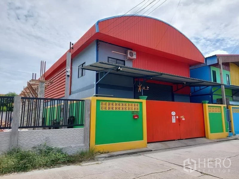 Warehouse for rent or sale in Bang Bua Thong, Nonthaburi - Side view of the modern warehouse facade with covered loading canopy and solid red gate.