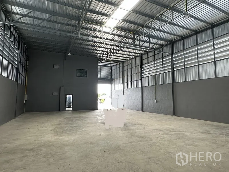 Warehouse for rent in Lam Luk Ka, Pathum Thani - Open warehouse hall with concrete floor, ventilation panels and large entry door.