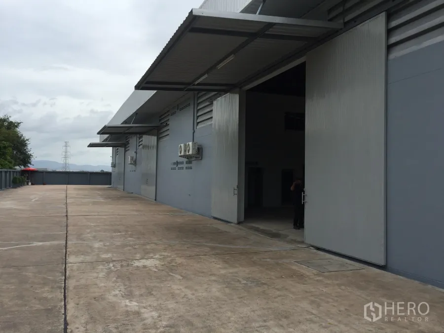 Factory for rent in Si Racha, Chon Buri - Exterior loading area with wide sliding metal doors, covered canopies, air-conditioning units and a broad concrete driveway.