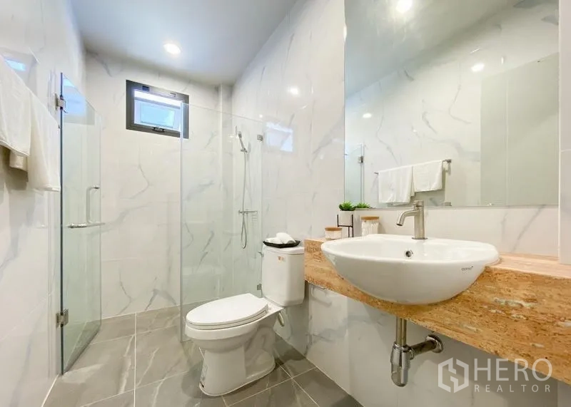 Detached House for sale in Lam Luk Ka, Pathum Thani - Bathroom with glass-enclosed shower, large mirror, and marble-look wall tiles.