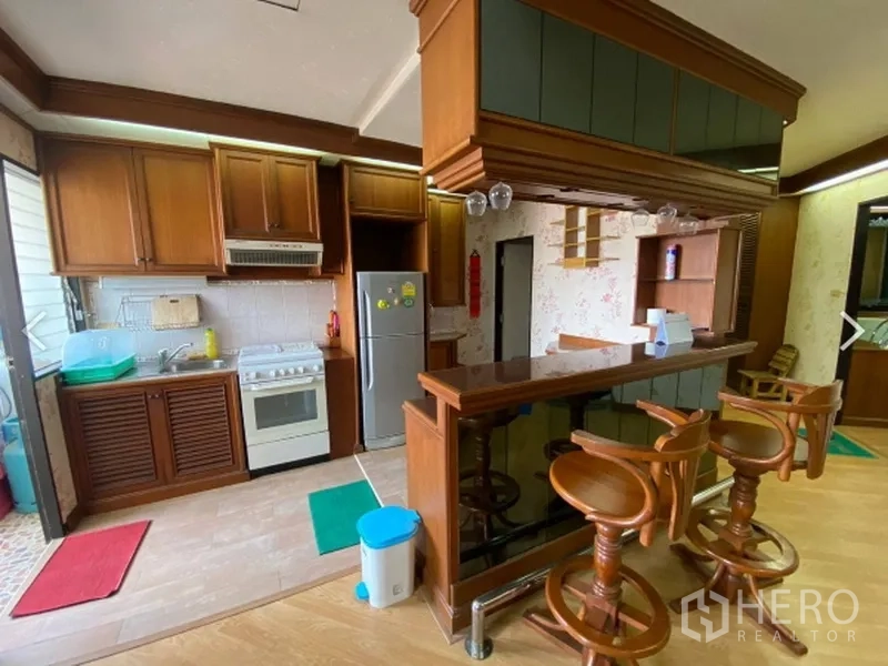 Condominium for sale in Watthana, Bangkok - Open kitchen with wood cabinets, breakfast bar and stools, stove and refrigerator at D.S. Tower 2 condo in Watthana.