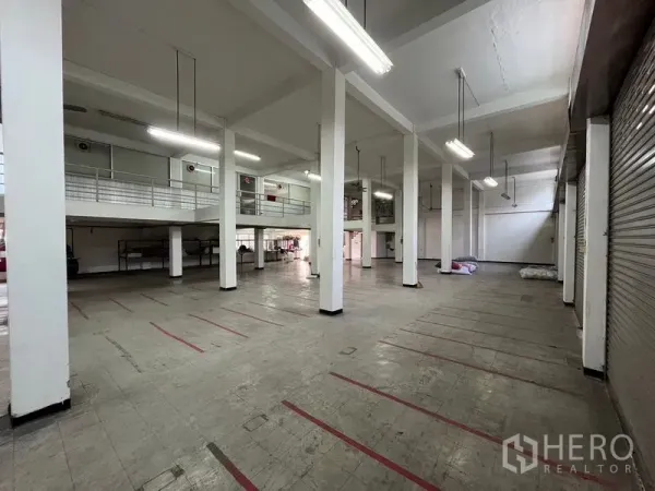 Shophouse for rent in Khlong Toei, Bangkok - High-ceiling ground floor hall with mezzanine level, strip lighting and roller shutters ideal for loading.