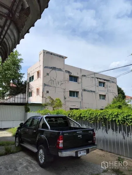 Warehouse for rent in Bueng Kum, Bangkok - Three-storey industrial building exterior with fenced yard and parking under a blue sky.