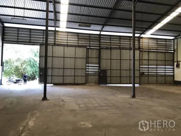 Warehouse for rent in Lam Luk Ka, Pathum Thani - Wide sliding metal doors and loading access inside a high-clearance warehouse with ventilation louvers.