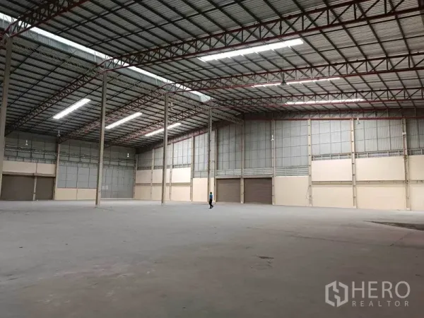 Factory for rent in Samut Prakan - Expansive factory warehouse in Bang Phli with high steel-truss ceiling, bright strip lighting, concrete floor and multiple roller-shutter bays.