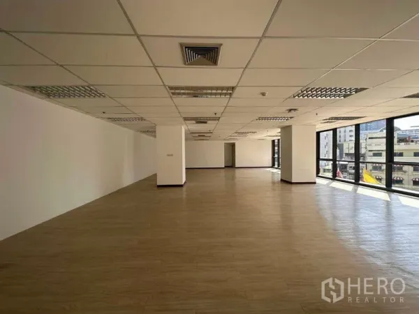 Office Space for rent in Watthana, Bangkok - Spacious open-plan office with large windows, city views, wood-style flooring, and a suspended ceiling with air vents.