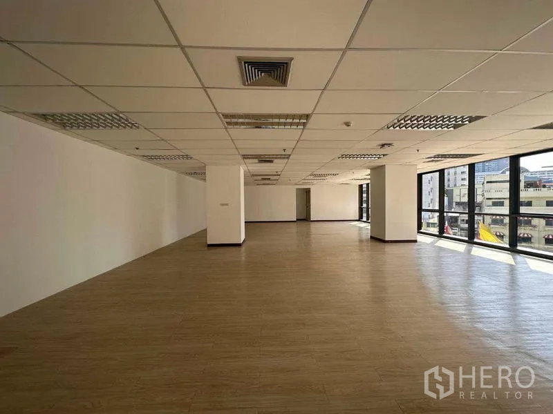Office Space for rent in Watthana, Bangkok - Spacious open-plan office with large windows, city views, wood-style flooring, and a suspended ceiling with air vents.