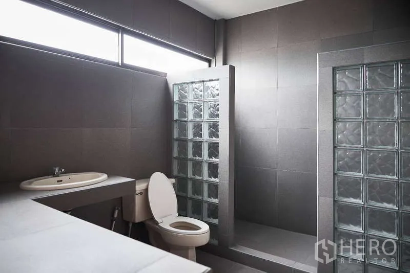 Townhouse for rent in Khlong Toei, Bangkok - Modern gray bathroom with glass‑block shower divider and window