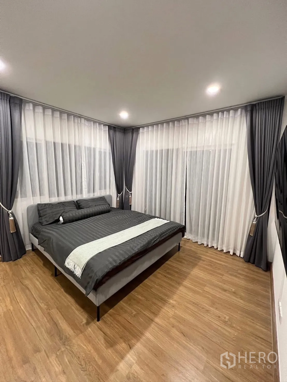 Detached House for rent in Prawet, Bangkok - Corner master bedroom with wraparound curtains, recessed lights and a queen bed.