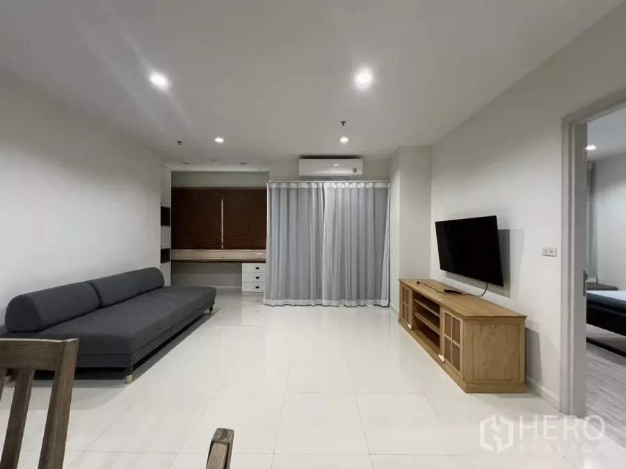 Condominium for rent in Bang Kapi, Bangkok - Bright living room with gray sofa, wall-mounted TV and built-in desk in a Bang Kapi condo.