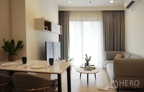 Condominium for rent in Pathum Wan, Bangkok - Cozy living room with dining nook, TV console, and balcony window with sheer curtains.