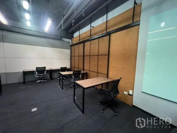 Office Space for rent - Open office zone featuring a cork accent wall, multiple desks and task chairs under linear ceiling lights.