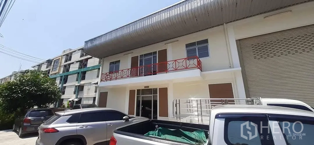 Factory for rent in Bang Sao Thong, Samut Prakan - Renovated factory frontage with red balcony railing, roller shutter door and parking bays.