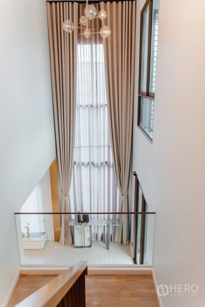 Detached House for sale in Bang Kapi, Bangkok - Staircase landing featuring a double-height window, glass railing and a modern chandelier that fills the space with natural light.