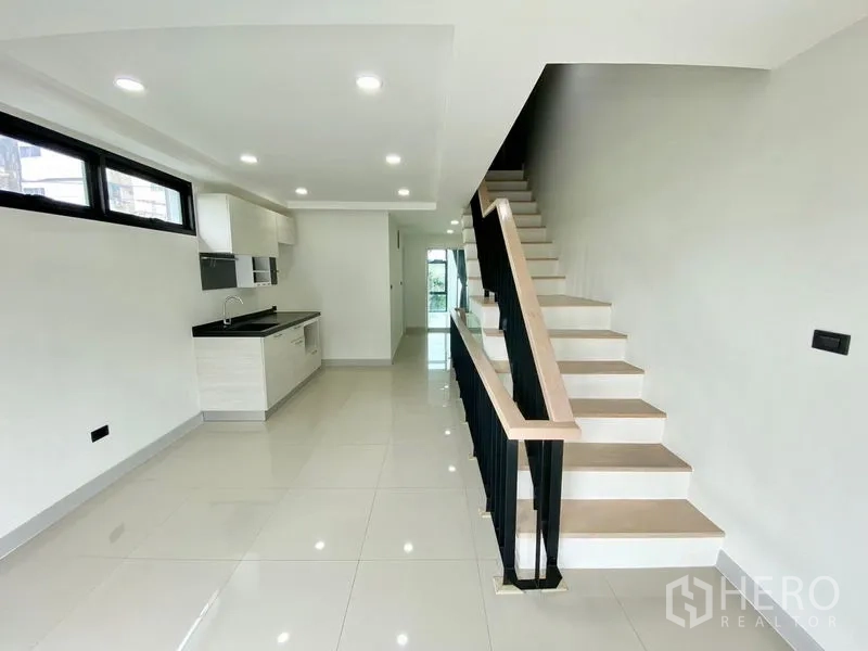 Home Office for rent or sale in Bang Na, Bangkok - Open-plan kitchen with white cabinetry beside a modern staircase and glossy tiled floors.