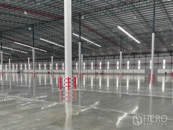 Factory for rent in Si Racha, Chon Buri - Column lines with red guards, strip windows and high‑bay LEDs across the factory floor.