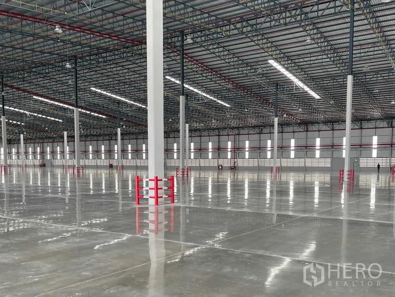 Factory for rent in Si Racha, Chon Buri - Column lines with red guards, strip windows and high‑bay LEDs across the factory floor.