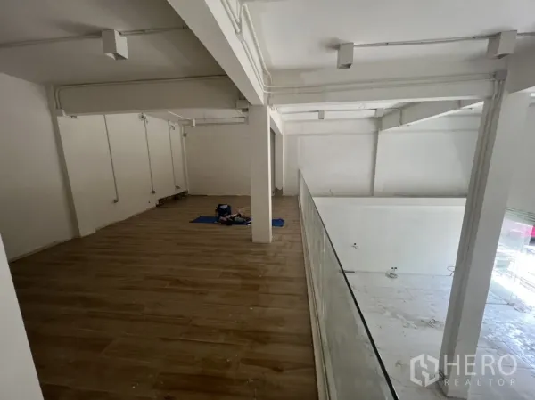 Shophouse for rent in Watthana, Bangkok - Mezzanine level with wood flooring and glass balustrade overlooking the showroom below.