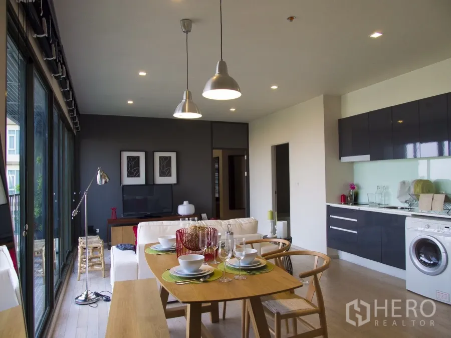 Condominium for rent in Watthana, Bangkok - Open-plan living and dining area with modern kitchen, floor-to-ceiling windows and pendant lighting.