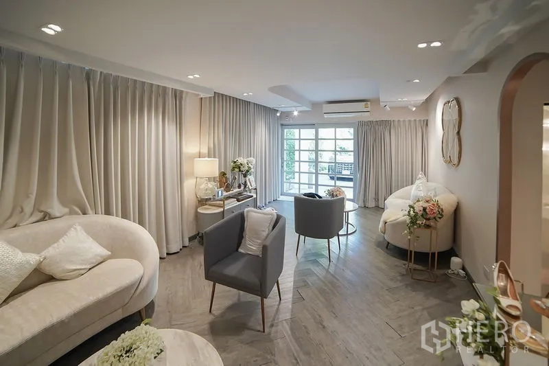 บ้าน ให้เช่าในHuai Khwang, Bangkok - เลานจ์อบอุ่น โซฟา ผ้าม่านสีเทา และประตูกระจกเปิดสู่ระเบียง
