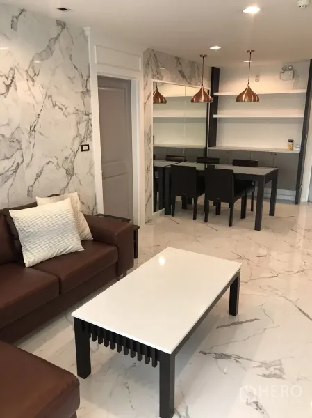 Condominium for rent or sale in Khlong Toei, Bangkok - Open-plan lounge connecting to dining area with marble-look finishes and copper pendant lights.
