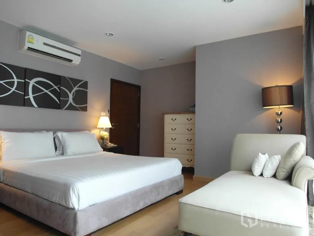 Condominium for rent or sale in Sathon, Bangkok - Spacious master bedroom with king bed, chaise lounge, soft lighting and grey accent walls.