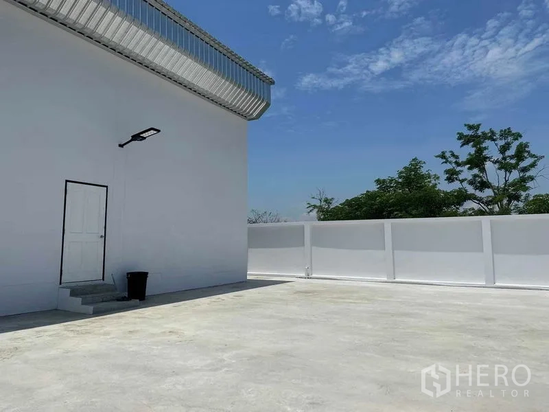Warehouse for sale in Khlong Luang, Pathum Thani - Back corner yard close-up showing white wall, service door and clear sky.