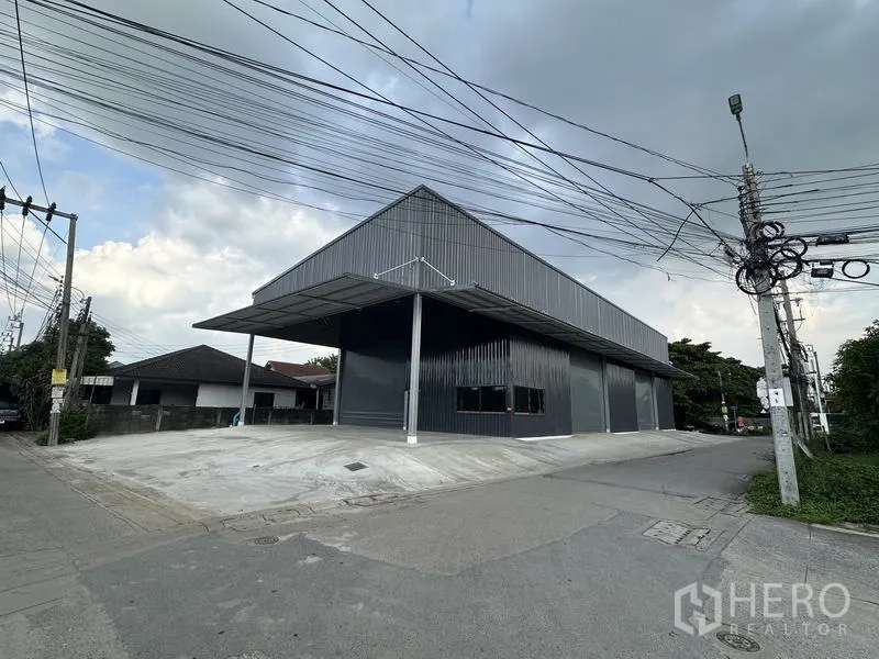 Warehouse for rent in Bang Kapi, Bangkok - Street perspective of the dark metal warehouse with covered dock and outdoor parking.