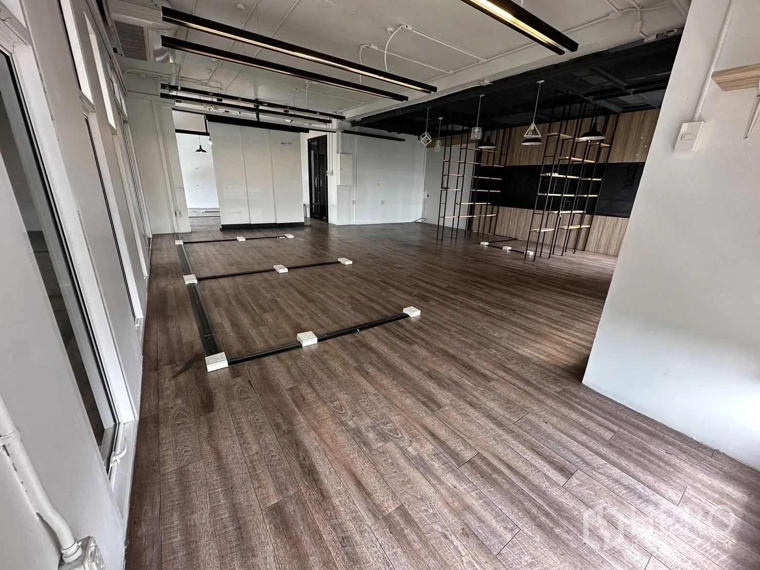 Office Space for rent in Watthana, Bangkok - Wide open office floor with floor outlet tracks, wood-style flooring, suspended lights, and a feature wall with shelving.