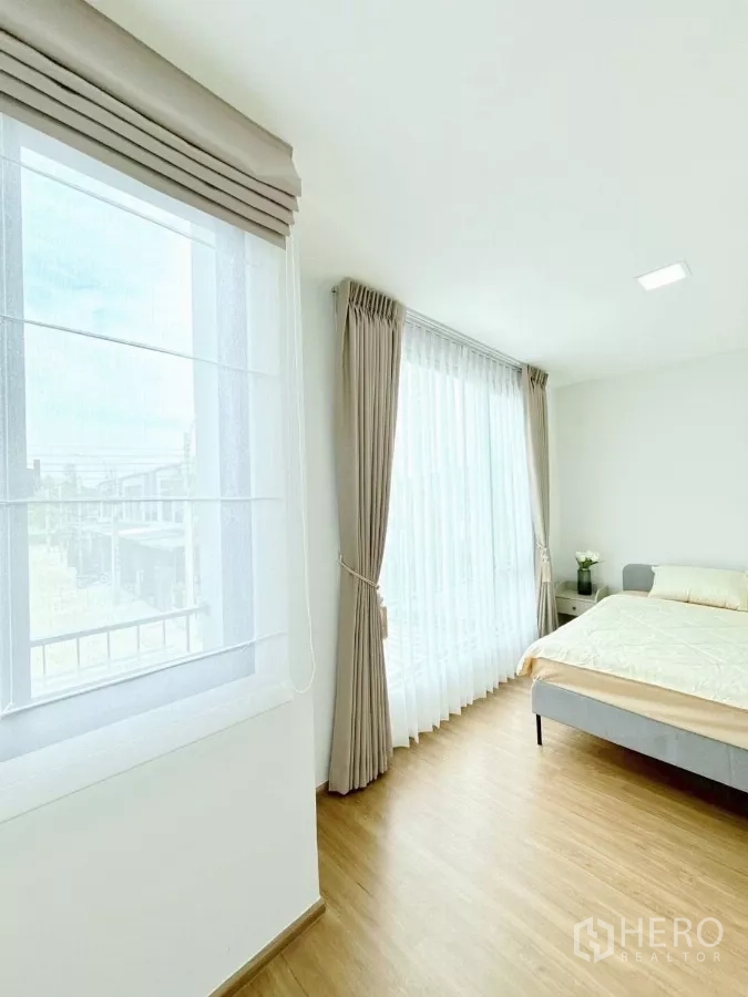 Townhouse for rent in Bang Phli, Samut Prakan - Sunlit master bedroom with corner windows, curtains and wood flooring.