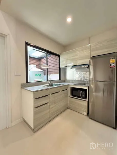Townhouse for rent in Bang Phli, Samut Prakan - Compact L-shaped kitchen with window, sink, microwave and fridge.