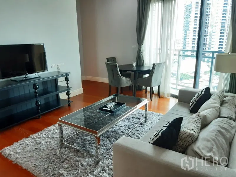 Condominium for rent or sale in Khlong Toei, Bangkok - Living room with TV console, round dining table by the balcony and skyline view.