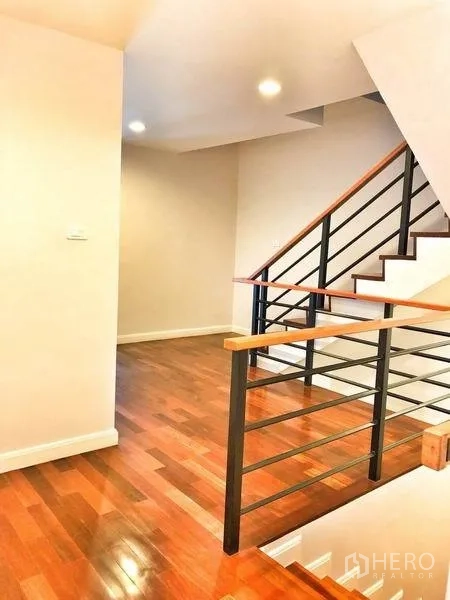 Townhouse for rent in Watthana, Bangkok - Upper-floor landing with metal handrail and wooden stairs.