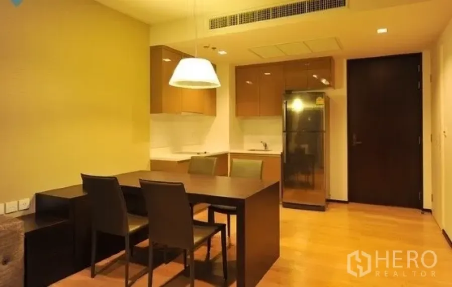 Condominium for rent in Khlong Toei, Bangkok - Open-plan dining area with dark wood table, pendant lamp, and a modern kitchenette backdrop.
