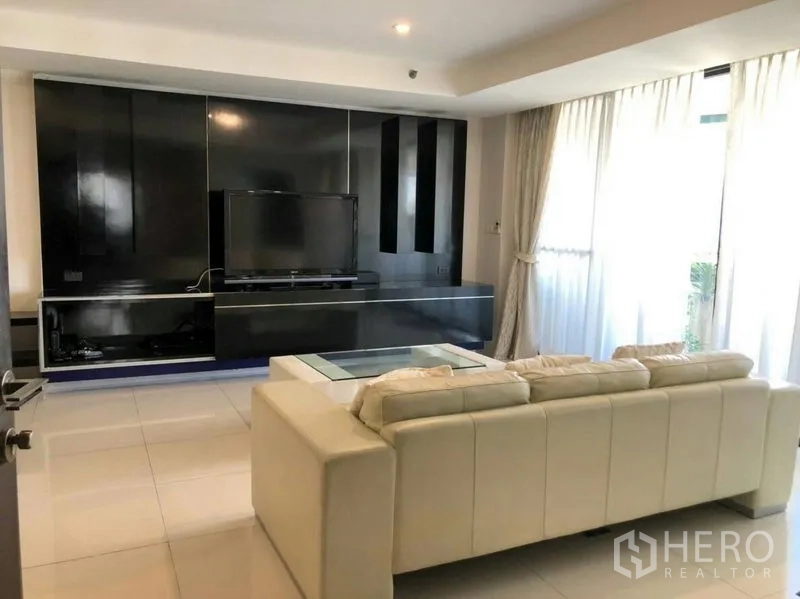 Condominium for rent or sale in Watthana, Bangkok - Living room with cream leather sofa, glossy media wall and floor-to-ceiling windows.