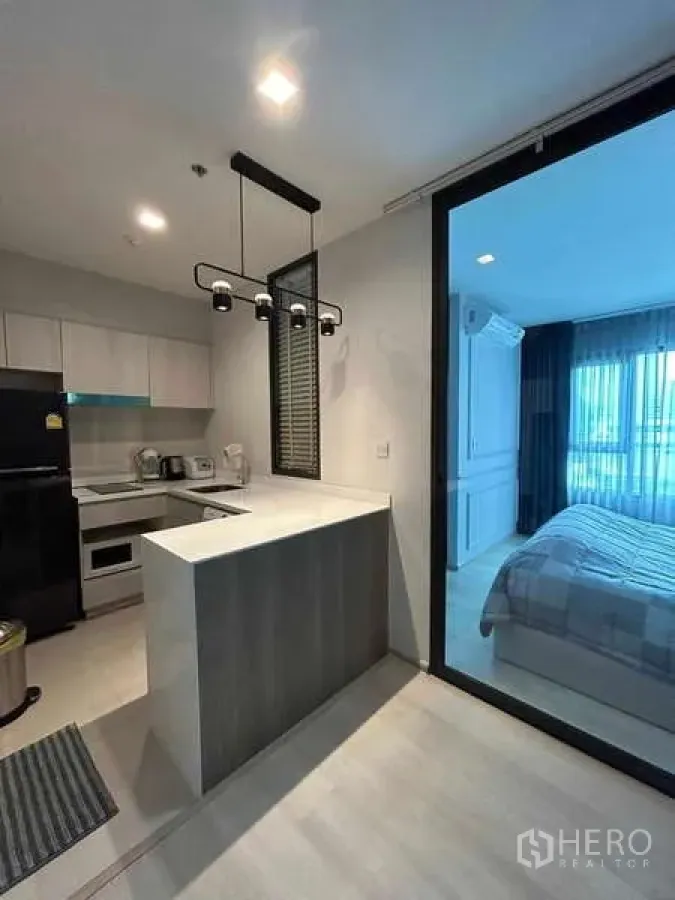 Condominium for sale in Pathum Wan, Bangkok - Modern kitchenette with appliances and island counter next to the bedroom entrance.