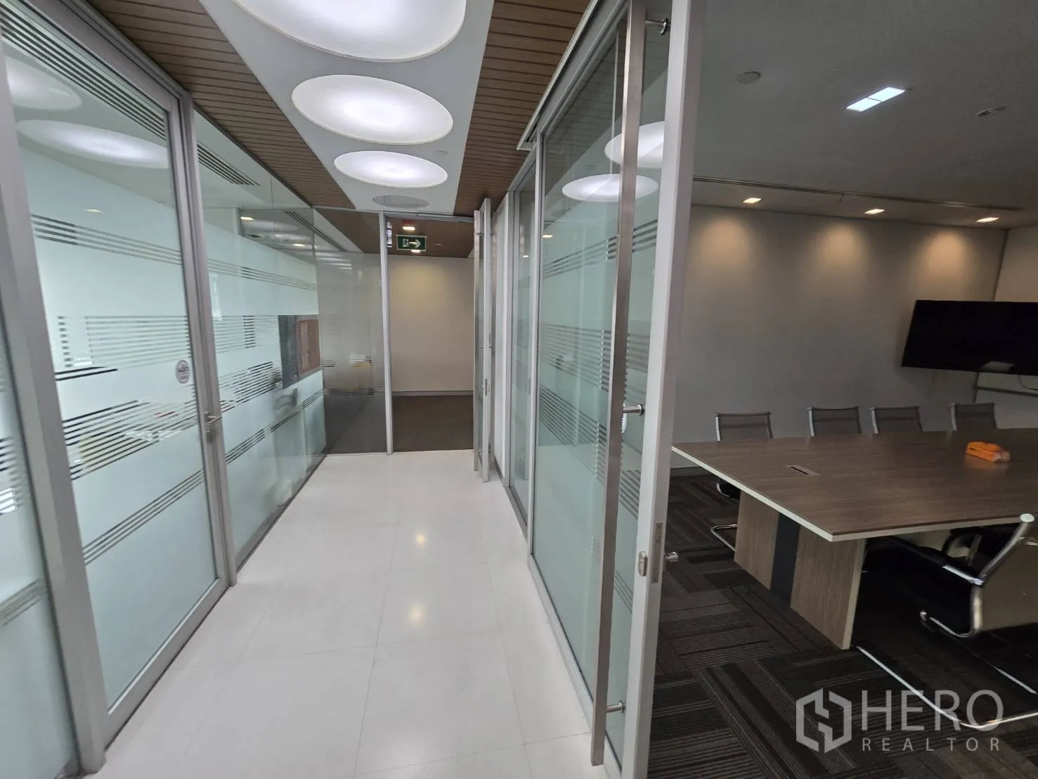Office Space for rent in Watthana, Bangkok - Corridor with glass partitions leading to meeting rooms under circular lights.